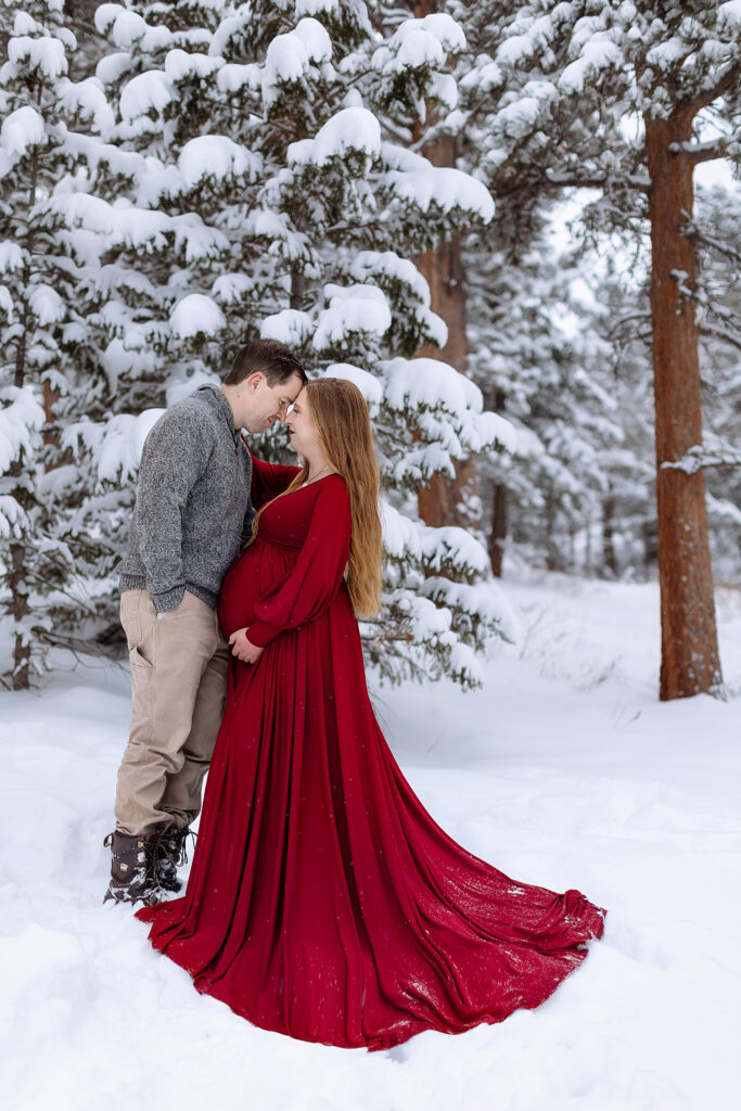 Family maternity photography in the snow-covered mountains of Estes Park, showing the intimate connection between parents-to-be and their growing family.