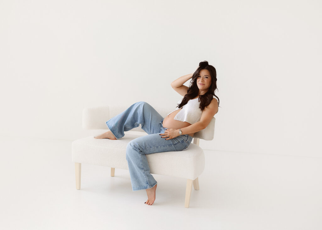 stunning mom to be on white couch in denver natural light studio holding her baby bump