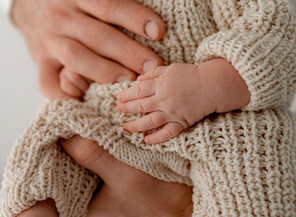 little hands resting on dads during a baby photoshoot in fort collins