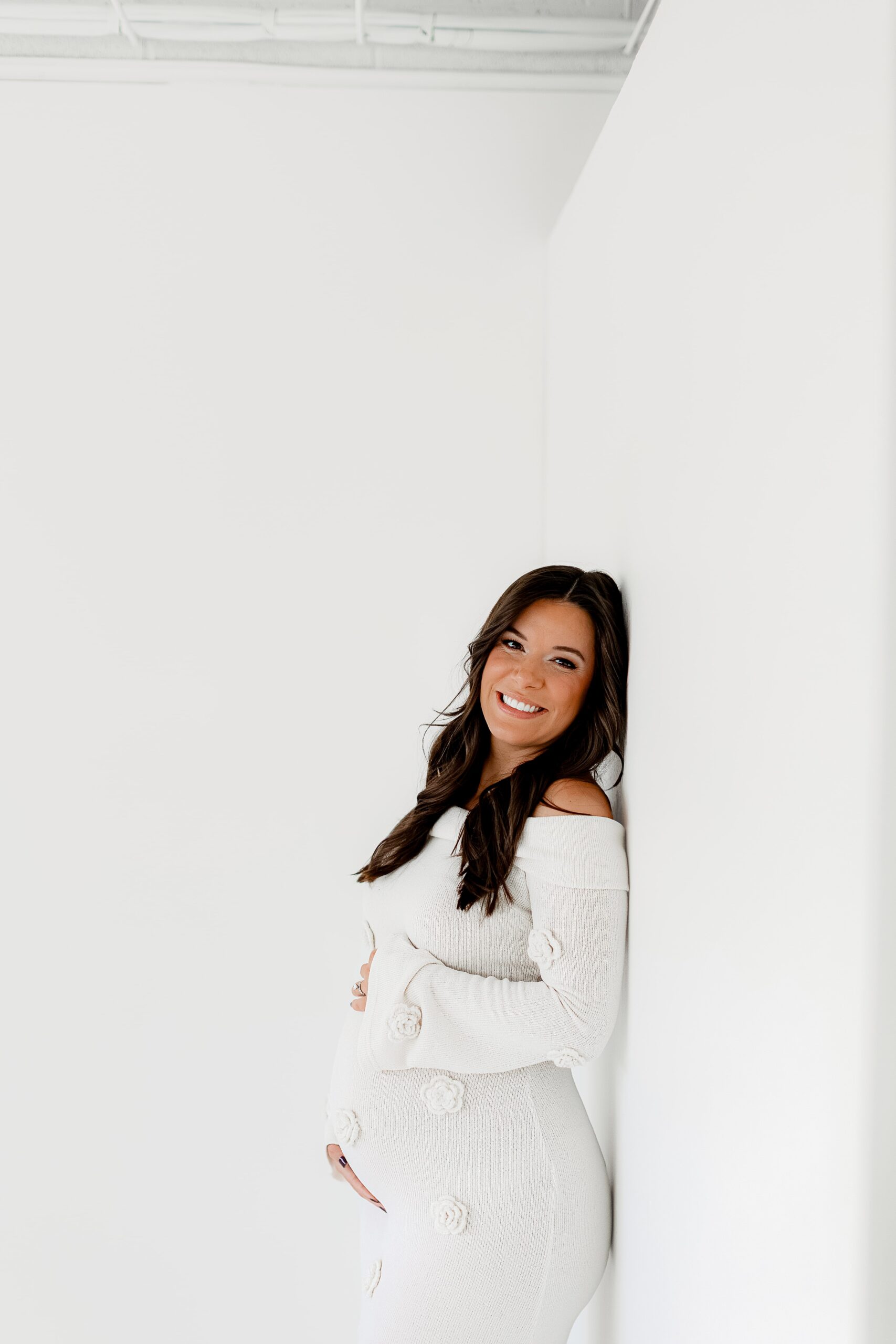 all white denver photography studio with a pregnant mom expecting her first baby in a white dress from her baby shower