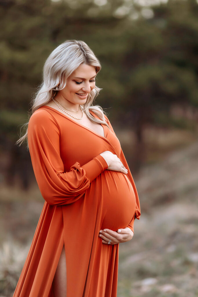 mom holding her baby bump at fort collins mountain location for photographer during their family photoshoot