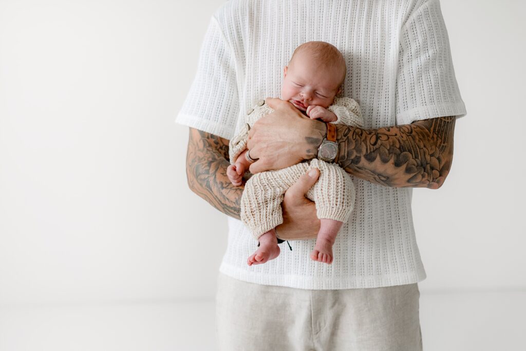 dad poses with his newborn baby son on his arm with his tattoos for a unique and personal close up during their family photos in boulder